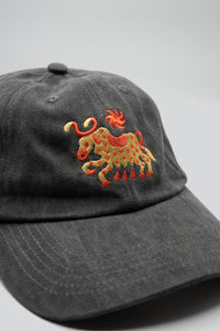 Gray dad hat with a horned cow and a sun embroidered in gold and red and "The Athletic" embroidered in the back