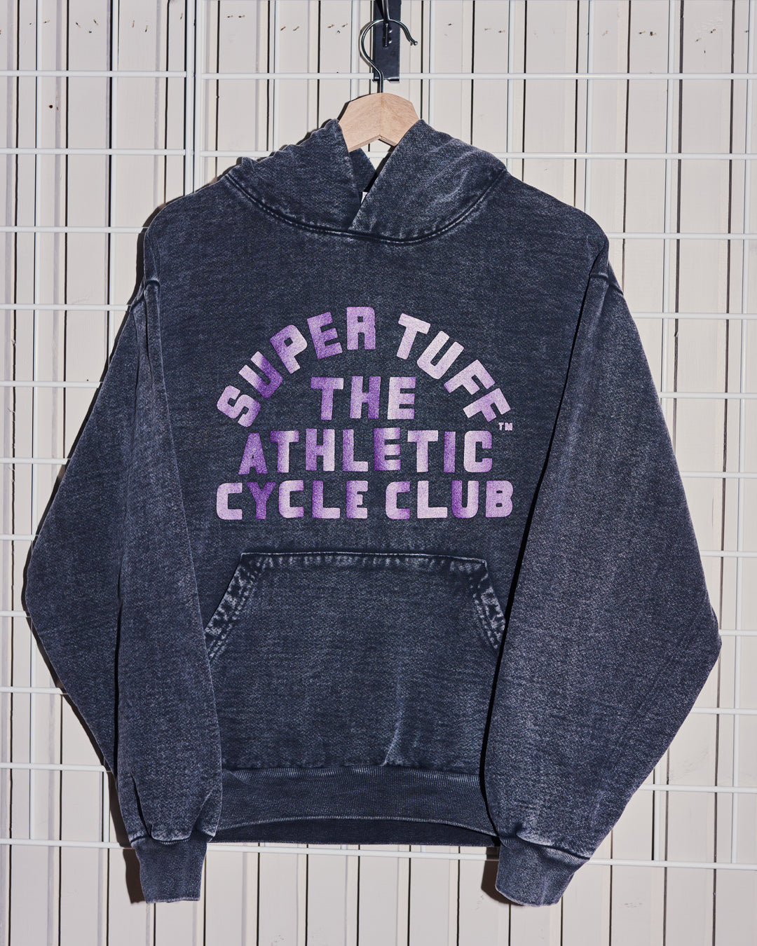 Black hoodie with 'Super Tuff The Athletic Cycle Club' text on a tiled wall background