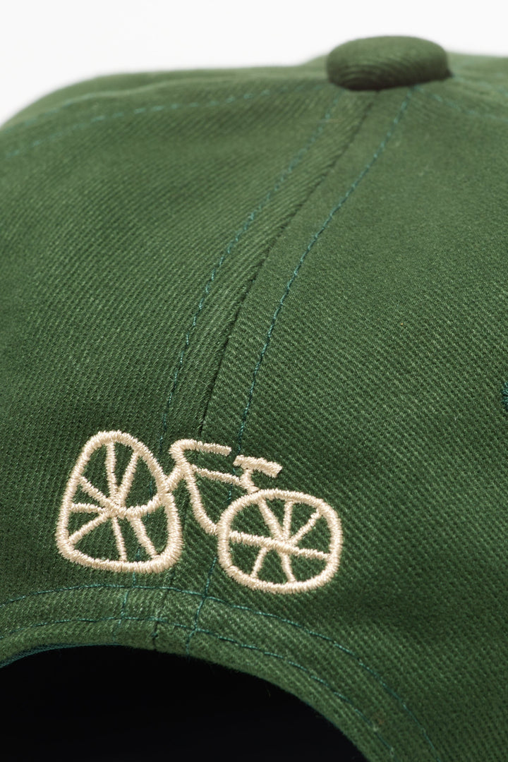 The I LIKE BIKE Hat is a green, 6-panel cap featuring the embroidered phrase "I LIKE BIKE" in white. It includes an adjustable fabric strap with a brass metal clasp for a customizable fit. Made from 100% cotton, this hat offers comfort and style for cycling enthusiasts