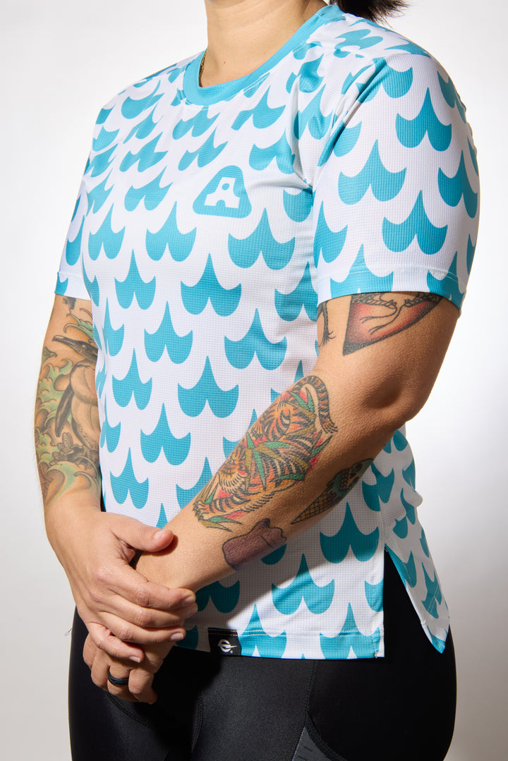 The Women's Mustache Tech Tee is a short-sleeve, moisture-wicking shirt designed for mountain biking, running, or road cycling. Made in the USA by Endo Customs, this versatile performance top adapts seamlessly to your ride or run. Constructed from lightweight, breathable Italian fabric, it features a split side seam at the hem to accommodate lower body movement