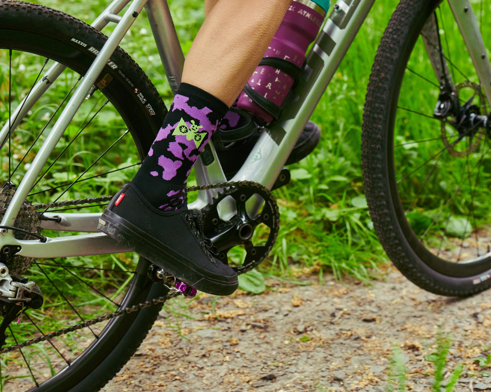 Person wearing black shoes with purple accents on a bicycle in a natural setting