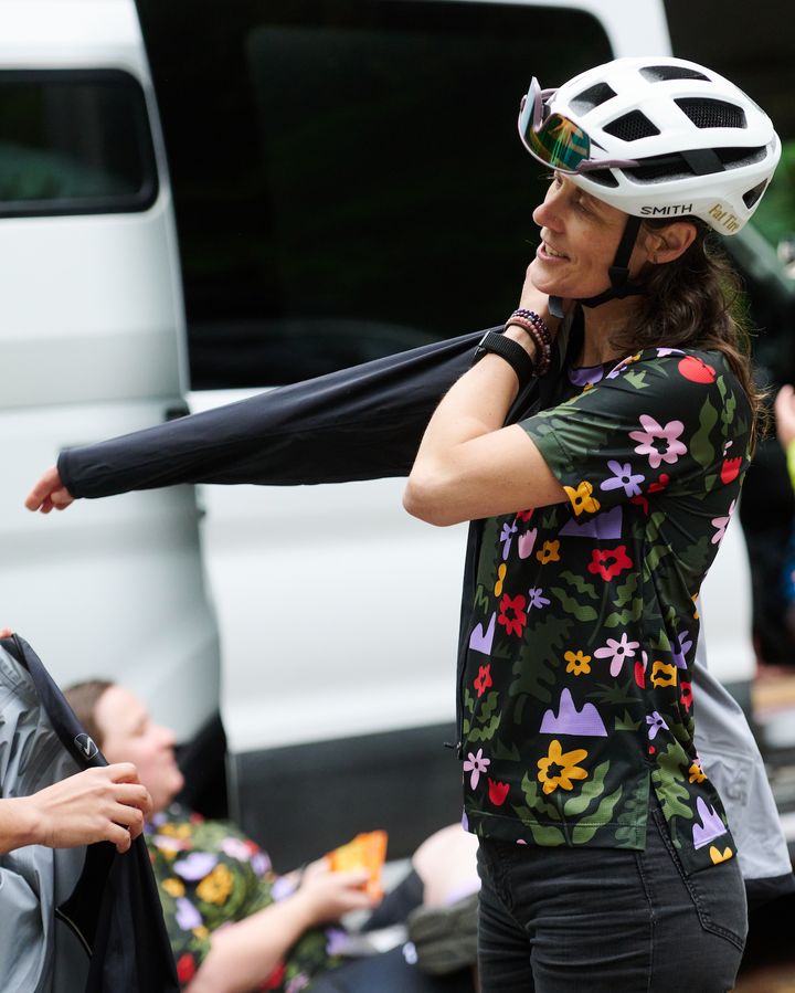 Person wearing a colorful floral-patterned shirt and helmet, standing in front of a white van.