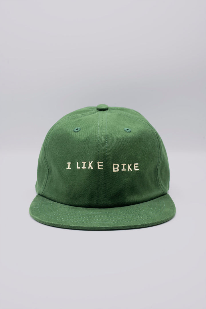 The I LIKE BIKE Hat is a green, 6-panel cap featuring the embroidered phrase "I LIKE BIKE" in white. It includes an adjustable fabric strap with a brass metal clasp for a customizable fit. Made from 100% cotton, this hat offers comfort and style for cycling enthusiasts