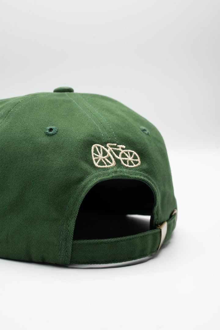 The I LIKE BIKE Hat is a green, 6-panel cap featuring the embroidered phrase "I LIKE BIKE" in white. It includes an adjustable fabric strap with a brass metal clasp for a customizable fit. Made from 100% cotton, this hat offers comfort and style for cycling enthusiasts