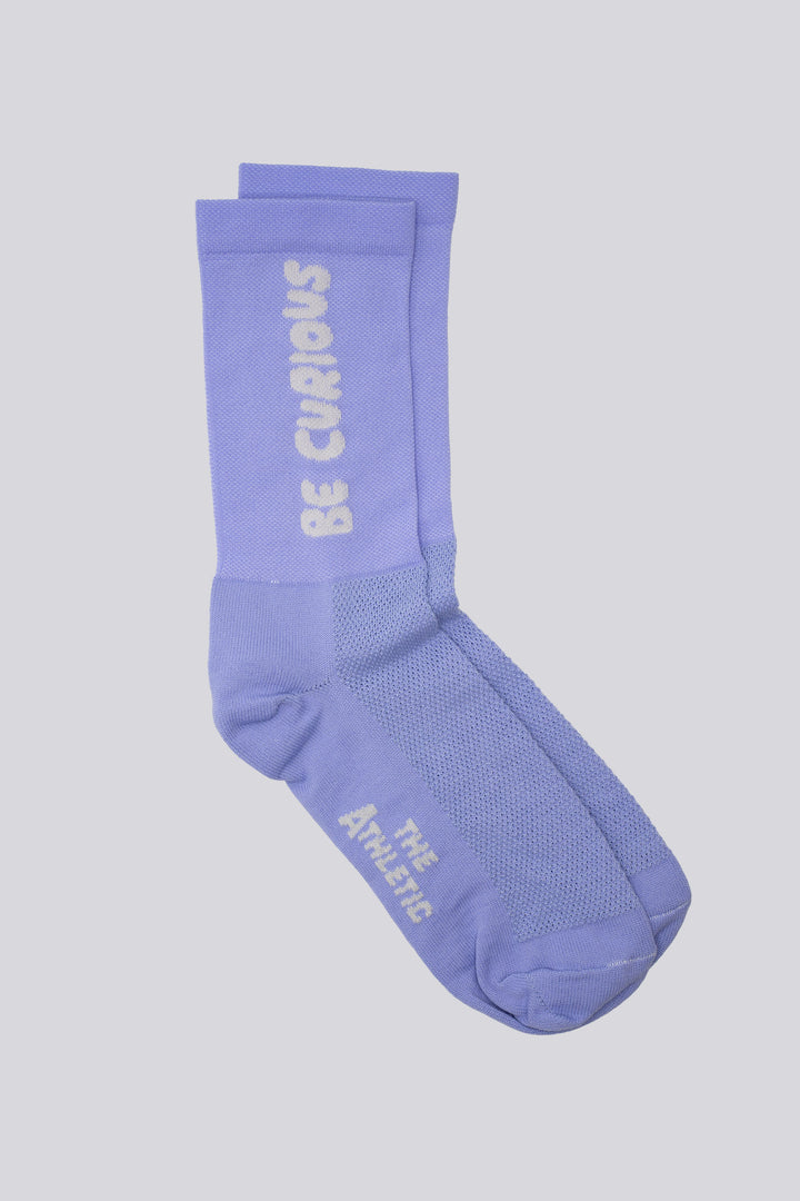 The Be Curious Socks are lavender socks featuring the phrase "Be Curious" on either side, designed for running and cycling. Perfect for cross-training, these socks combine style and performance. Please note that this item is on final sale and is not eligible for returns or exchanges