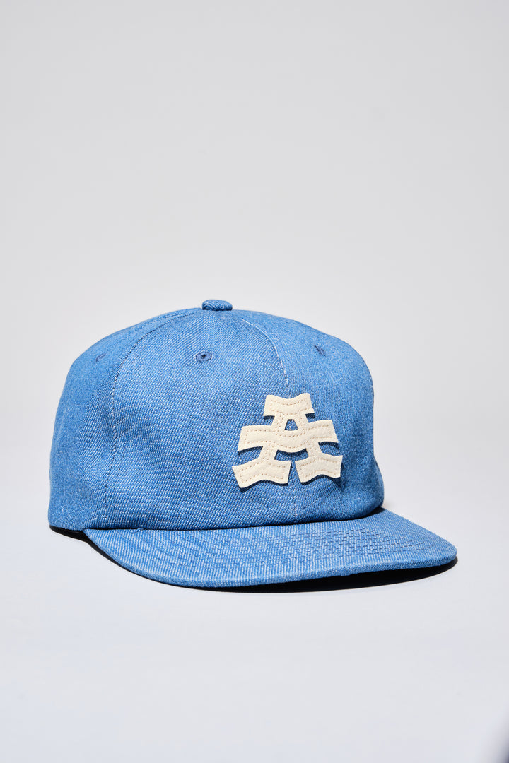 The Athletic Wavy A Denim Hat is a 100% cotton denim cap featuring the embroidered "Wavy A" logo, symbolizing The Athletic's blend of past and future. Designed in collaboration with Young Jerks, this hat offers a timeless, denim aesthetic suitable for various off-bike activities