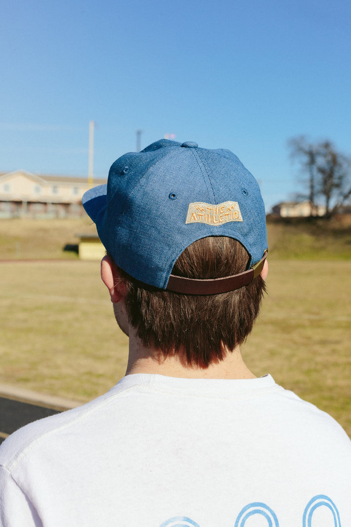 The Athletic Wavy A Denim Hat is a 100% cotton denim cap featuring the embroidered "Wavy A" logo, symbolizing The Athletic's blend of past and future. Designed in collaboration with Young Jerks, this hat offers a timeless, denim aesthetic suitable for various off-bike activities