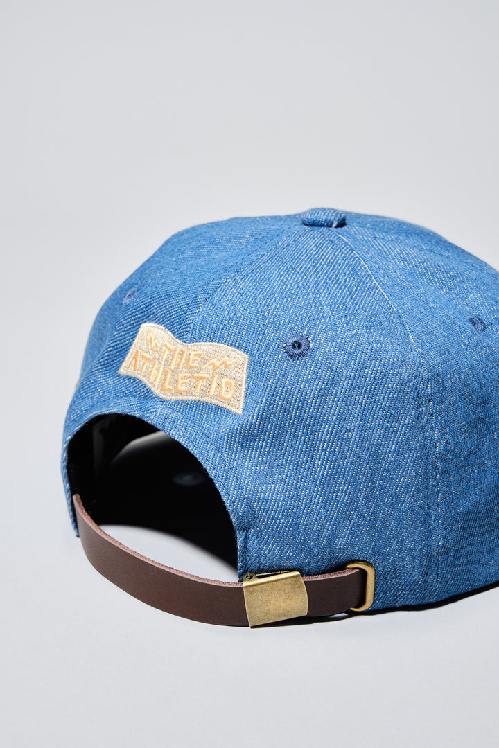 The Athletic Wavy A Denim Hat is a 100% cotton denim cap featuring the embroidered "Wavy A" logo, symbolizing The Athletic's blend of past and future. Designed in collaboration with Young Jerks, this hat offers a timeless, denim aesthetic suitable for various off-bike activities
